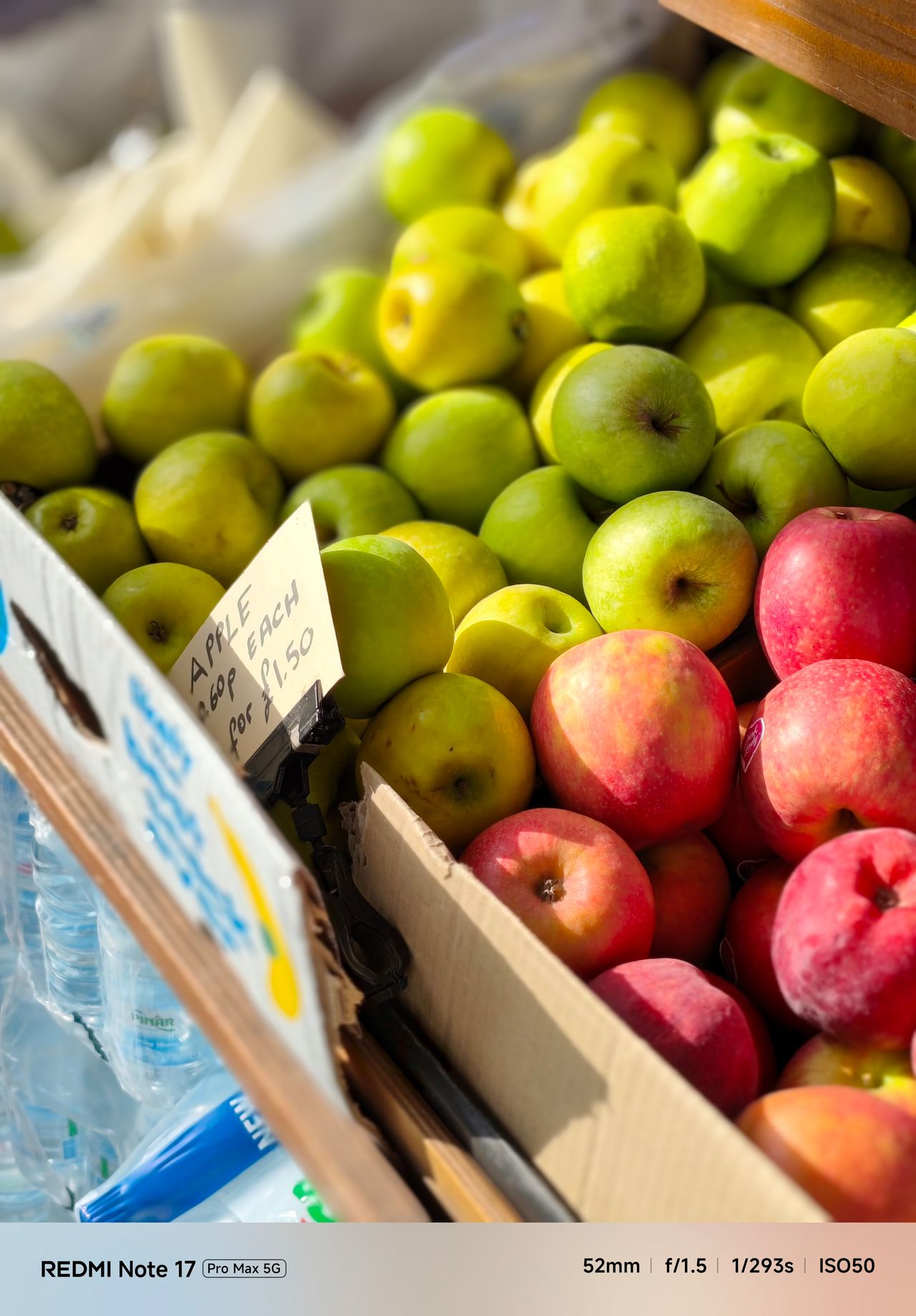 Red and green apples at a market stall with simulated shallow depth of field blurring the background.