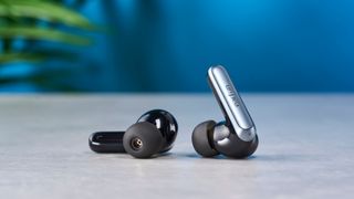 a pair of silver and black shiny earbuds with a black matte charging case are photographed against the Tom's Guide blue background