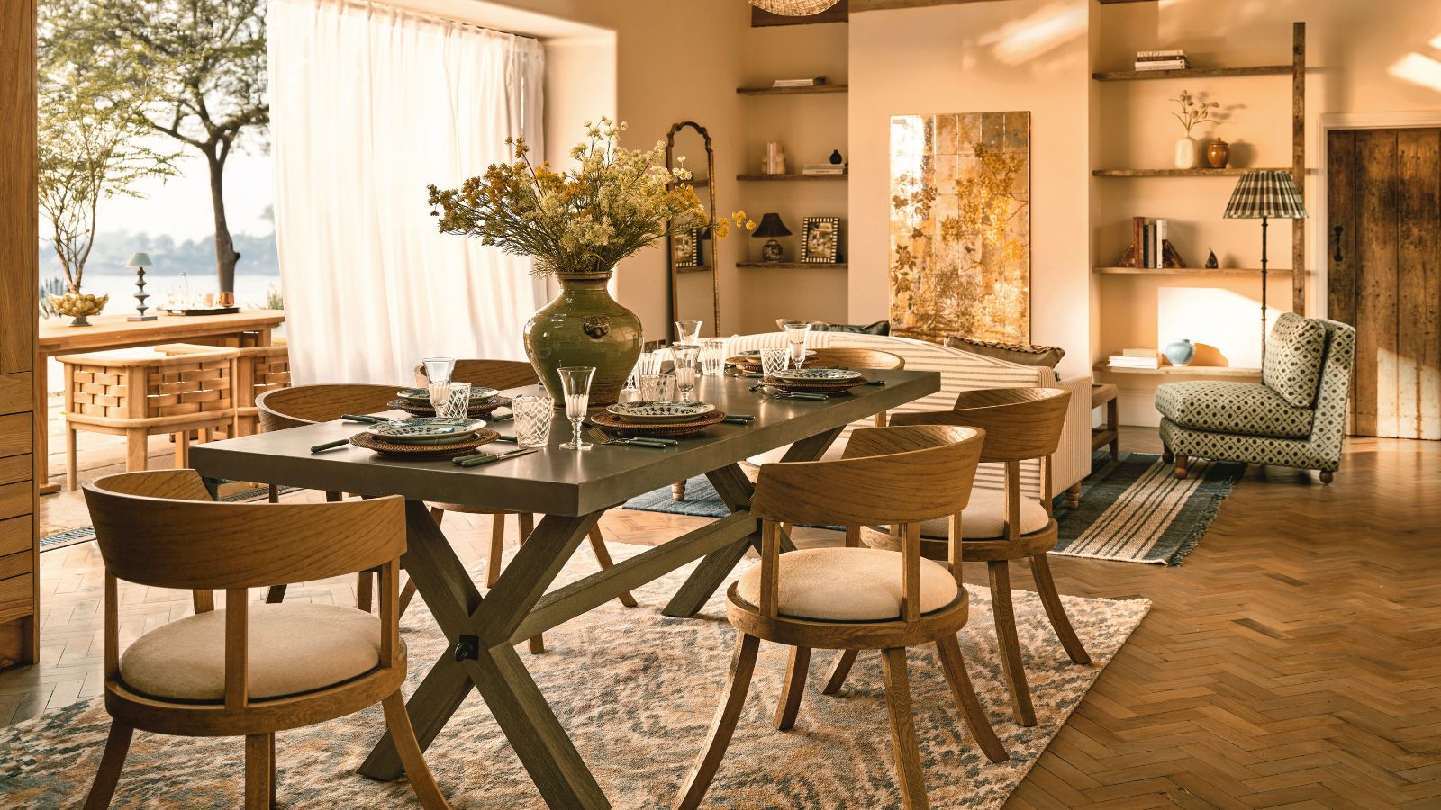 A warm-toned living dining room, with a large black table with six chairs around it. A large bi-folding door behind the table opening out onto a sunny patio. 