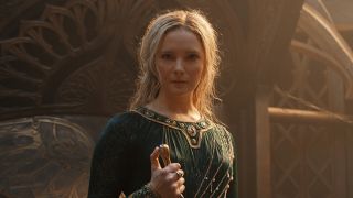 Morfydd Clark holding a weapon in front of an ornate backdrop in The Lord of the Rings: Rings of Power.