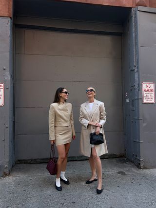 Anna LaPlaca and Kristen Nichols wearing beige outfits, black ballet flats, and Bottega Veneta bags