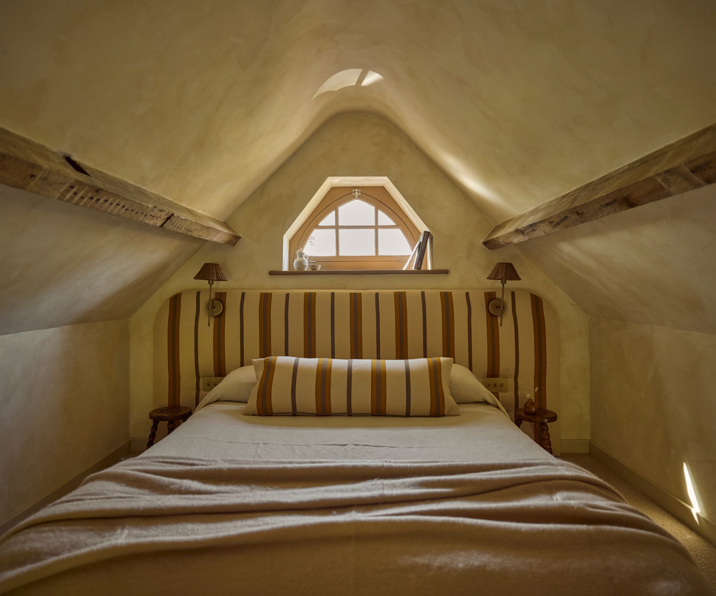 A tiny home bedroom with warm neutral lime wash walls, exposed wooden beams, and a striped headboard