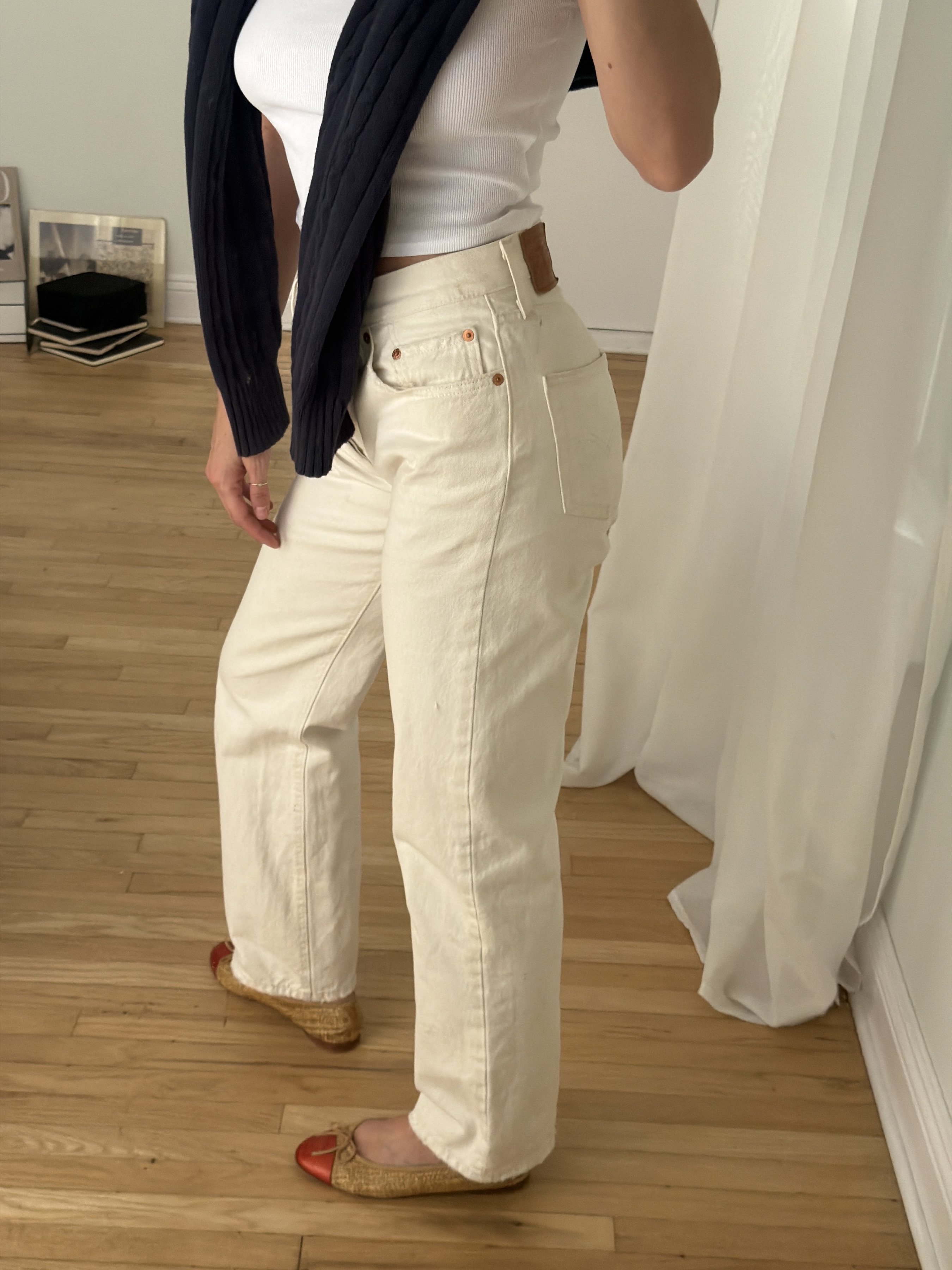 Kathryn Zahorak posing in mirror wearing white jeans, white t-shirt, navy sweater, and red cap ballet flats