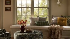 banquette window seat styled for fall with a green tapestry print armchair and ottoman, styled with a tray with books and a vase of orange dried flowers and a mix of fall pillows and blankets