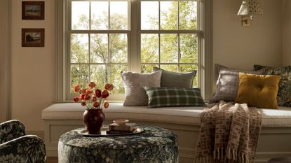 banquette window seat styled for fall with a green tapestry print armchair and ottoman, styled with a tray with books and a vase of orange dried flowers and a mix of fall pillows and blankets