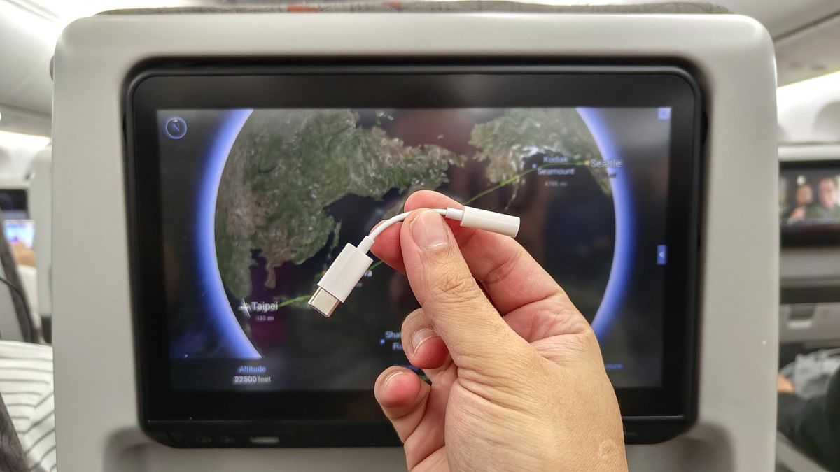 Apple&#039;s USB-C to 3.5mm headphone jack in front of a seat-back display on a plane