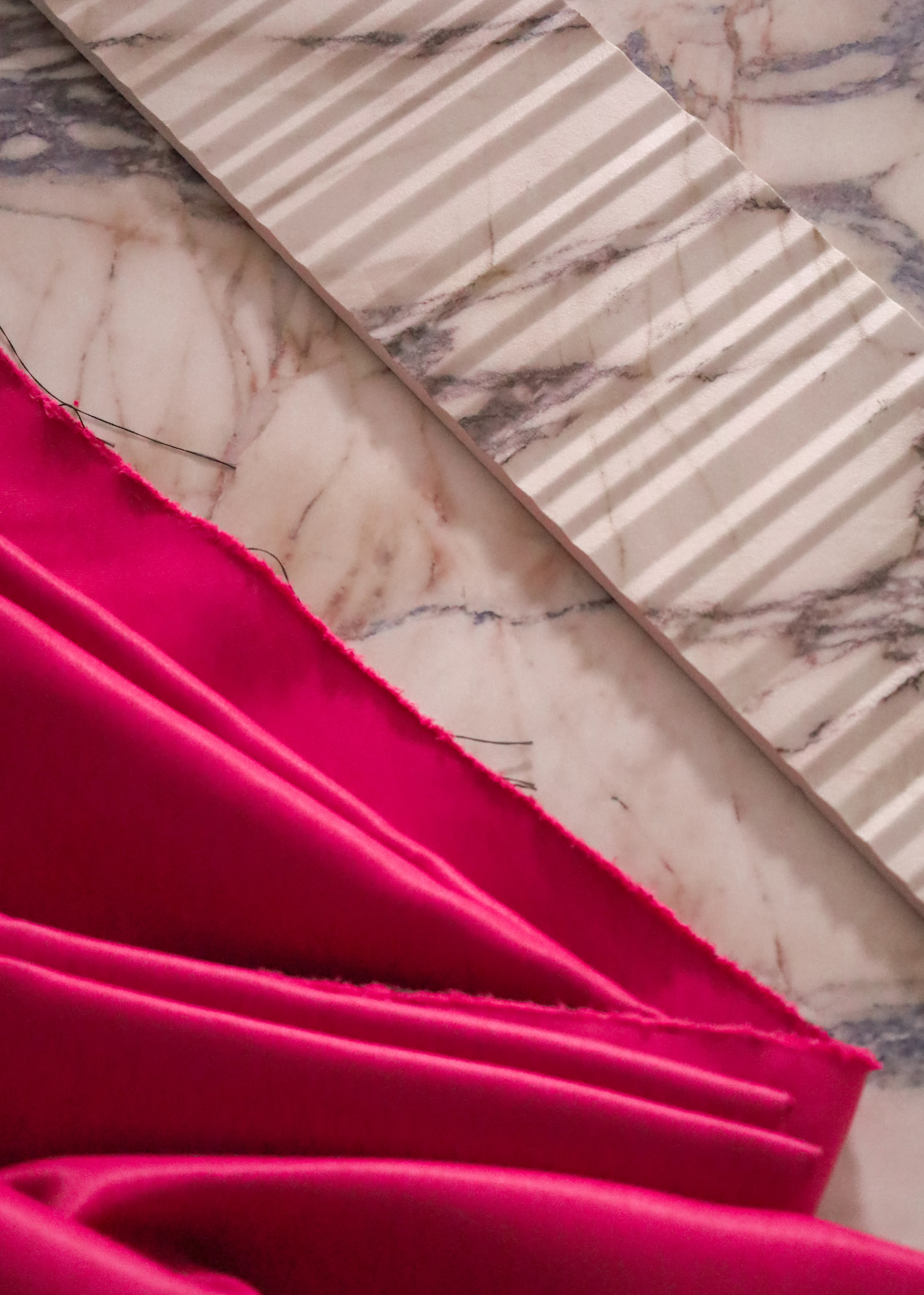 A close-up of a bright pink fabric on a marble table near a ridged marble slab