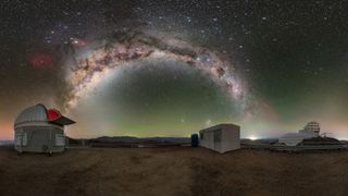 the bright band of the milky way arcs in the night sky over two observatory complexes in chile