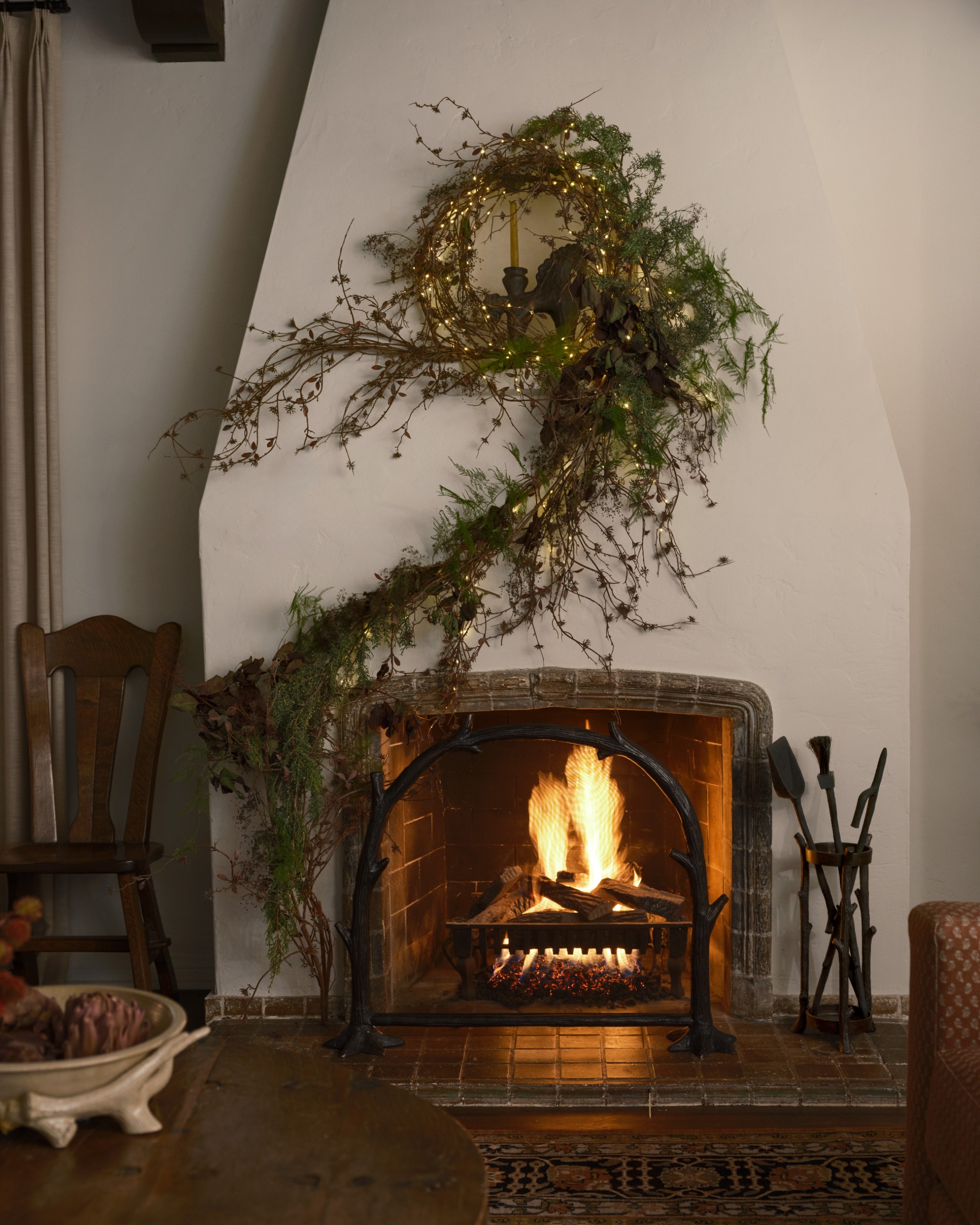 white plastered fireplace with a winding green foliage above and traditional accessories to the side