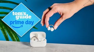 Soundcore Aeroclip earbuds in white and cold with one bud being held by a woman's hand in front of a blue background with a prime day tag. 