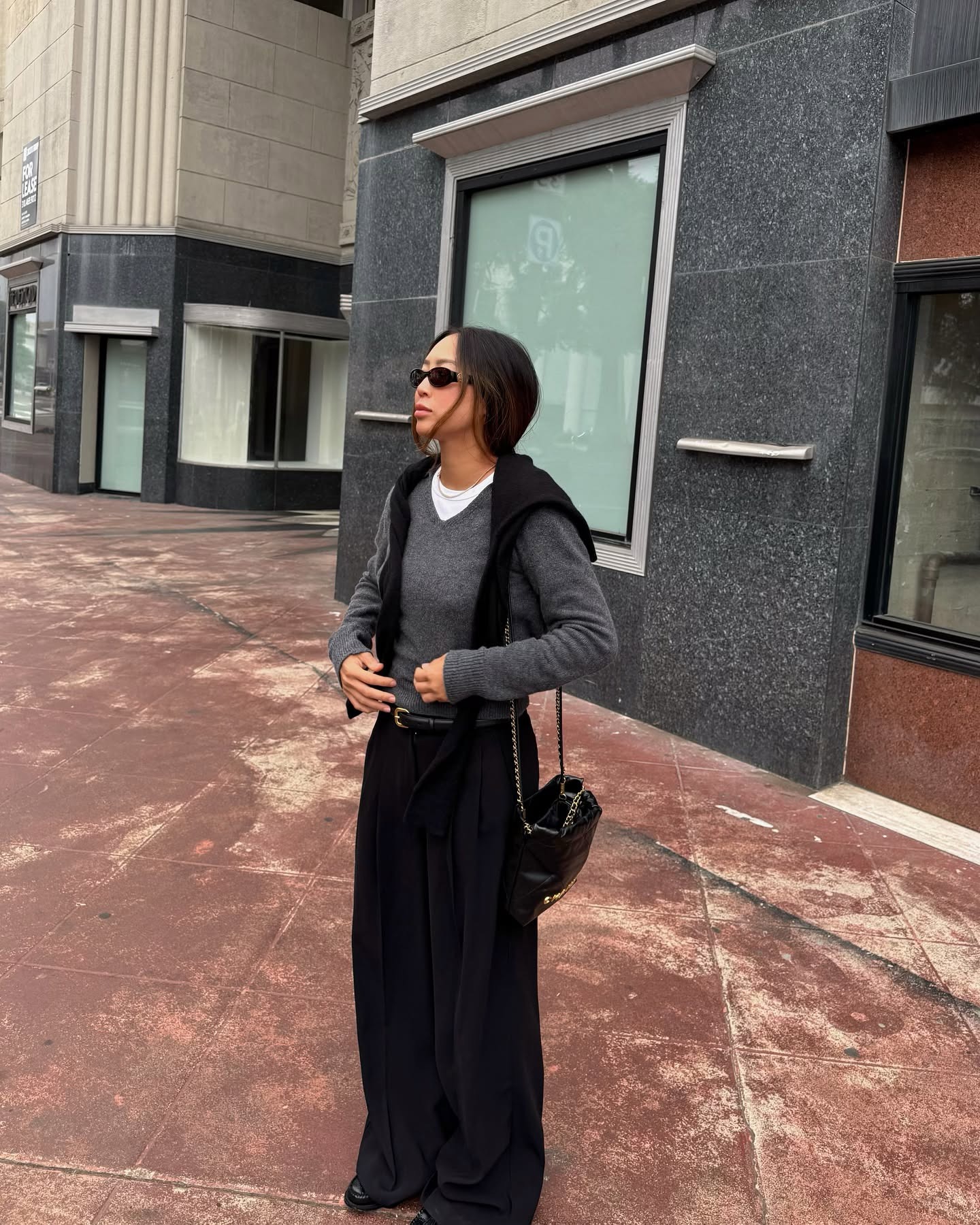 Woman in gray V-neck sweater and black pants.