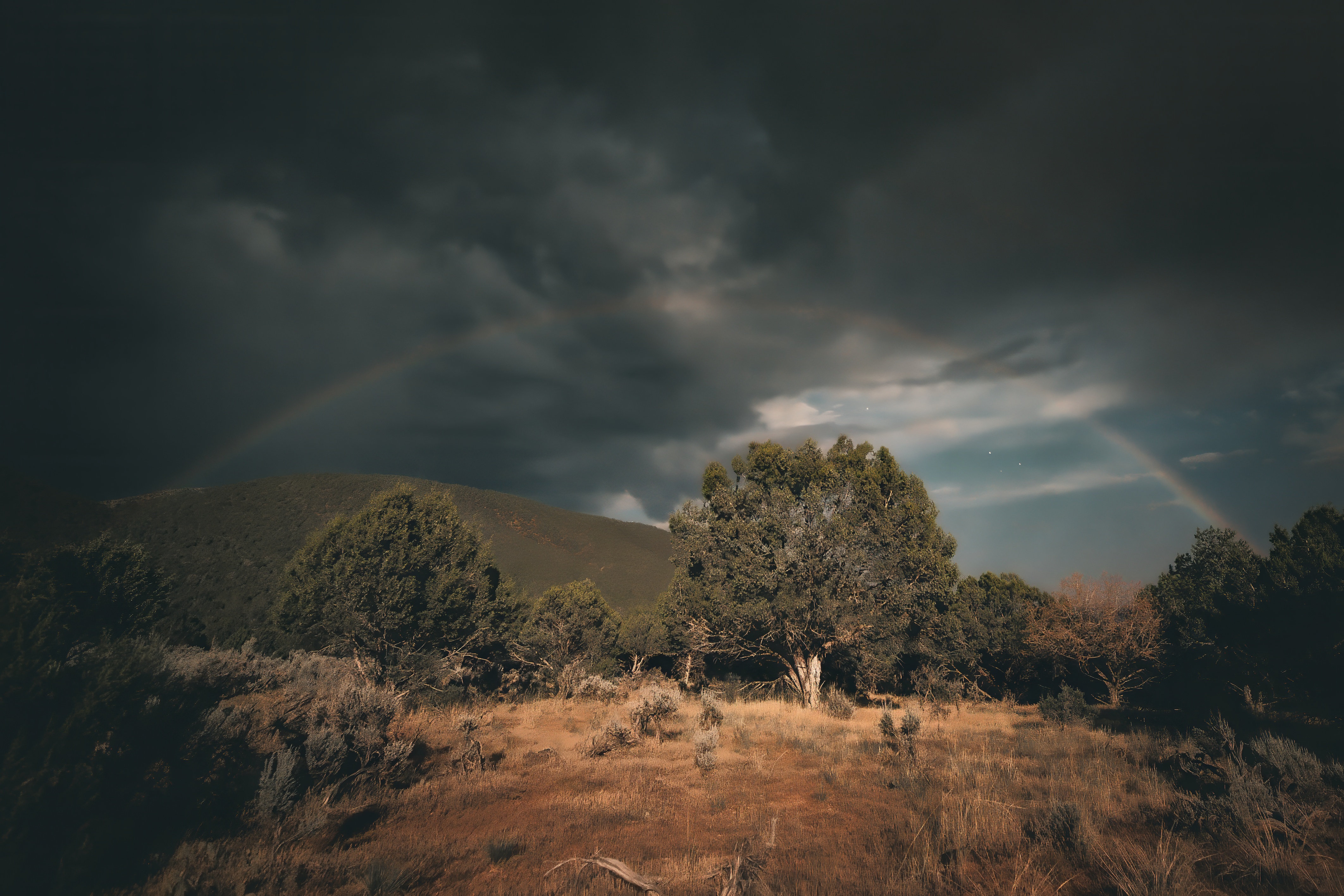 faint but colorful moonbow arches across the night sky filled with dark clouds.