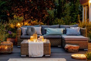 Outdoor rattan furniture in a leafy green garden, lit by candles.