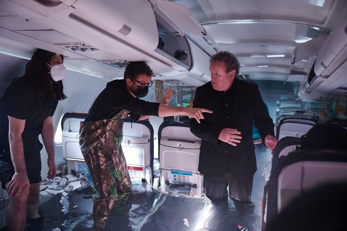 A behind-the-scenes image from Amazon Prime movie &#039;No Way Up&#039;, featuring actor Colm Meaney on set with the film crew, standing inside an airplane filling up with water