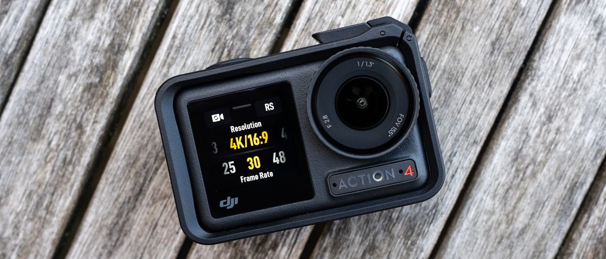 A small black camera on a faded wooden table. The left half of the camera is a simple digital screen. On the right side of the camera is the round lens and beneath that is the &#039;ACTION 4&#039; branding.