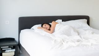 A woman sleeps on a mattress placed on a grey box spring