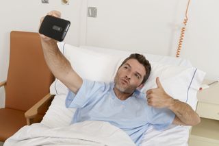 Man lying on hospital bed photographing himself in an amusing way