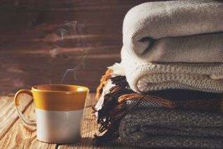 A cup of tea with a pile of cosy blankets.
