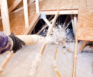 Someone spraying loose insulation into a floor cavity