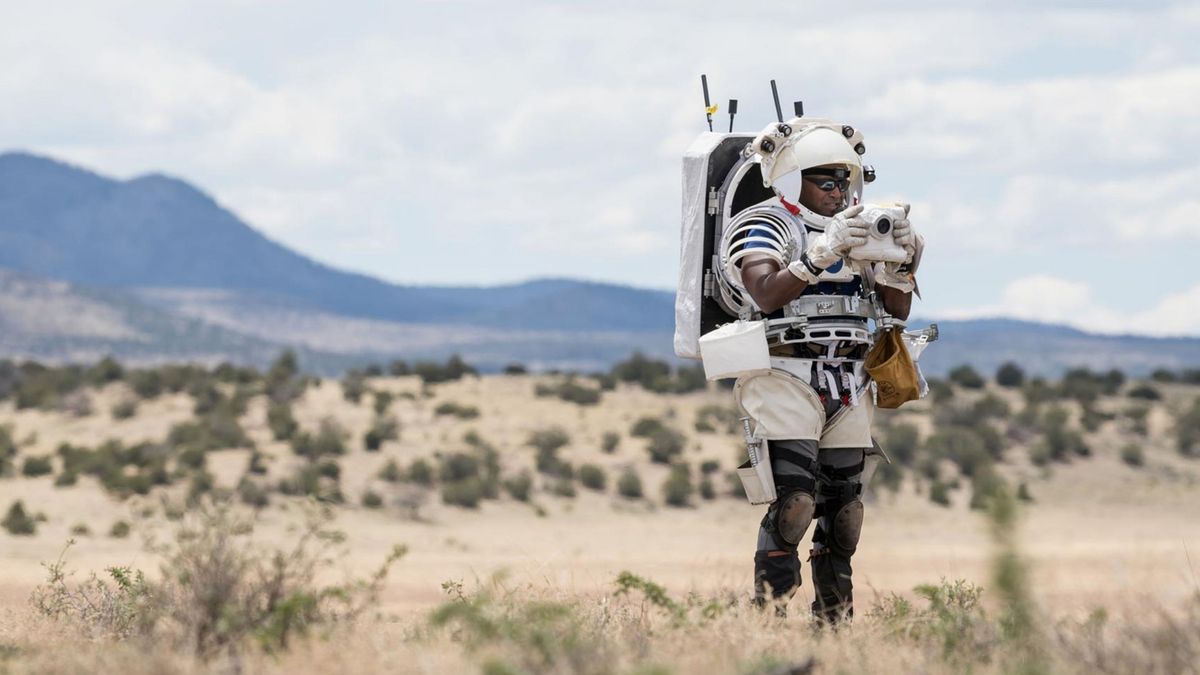 An astronaut in the desert wearing a space suit and using the Nikon Handheld Universal Lunar Camera (HULC)