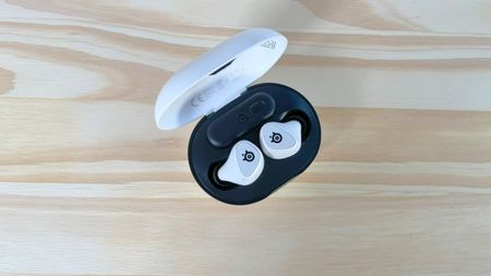 The SteelSeries Arctis GameBuds in their case on a wood table