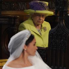 Queen Elizabeth wears a lime green outfit and looks at Meghan Markle who is wearing a veil and white wedding dress at her nuptials to Prince Harry on May 19, 2018