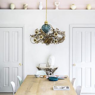 A white dining space with two doors, a blue pendant light and a wooden table