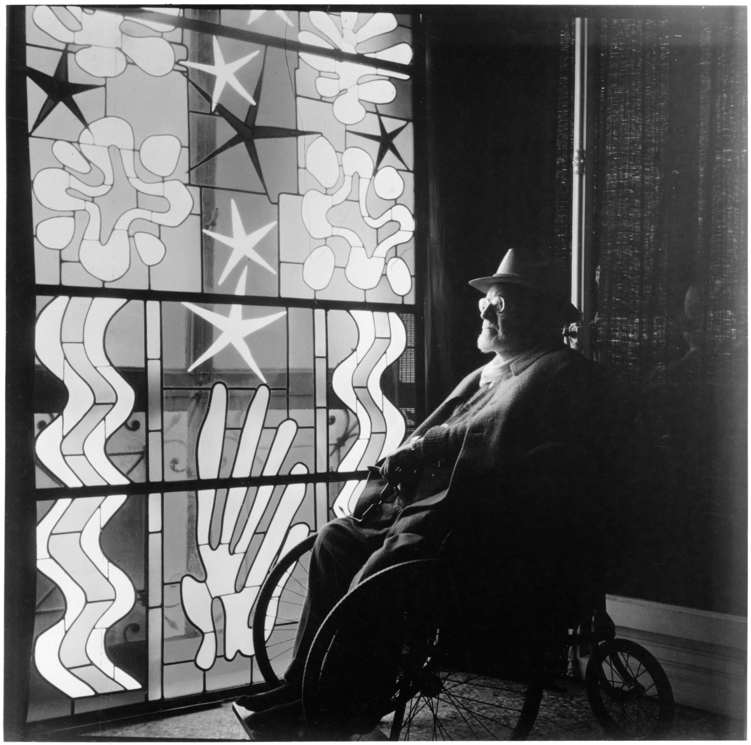 Henri Matisse in a wheelchair looking through a stained glass window