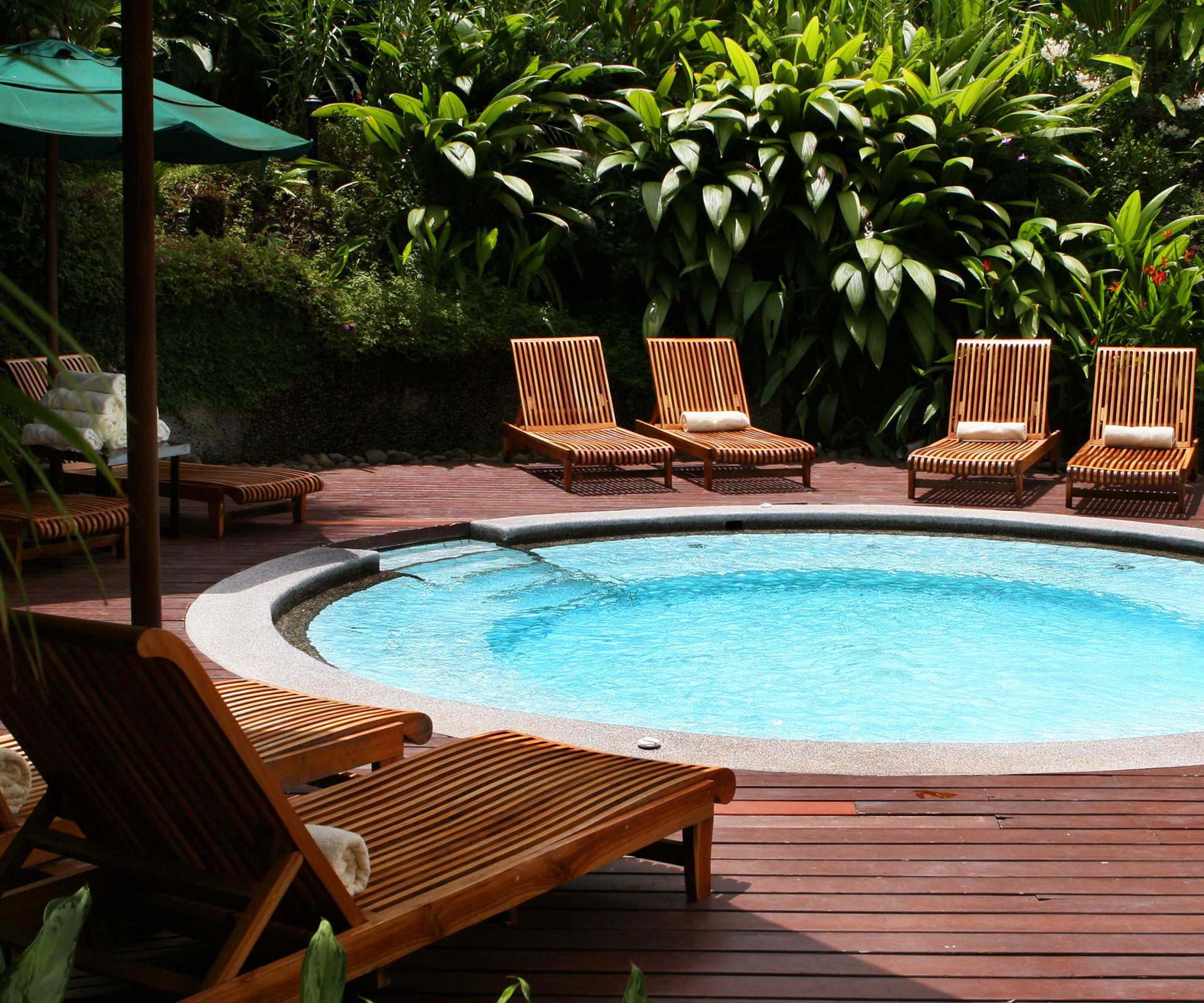 A circular pool recessed into a dark wood deck with sun loungers around