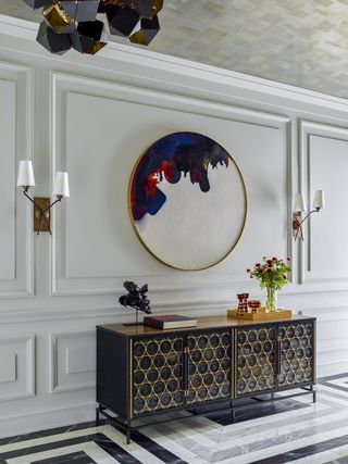 Entryway with dark blue console table adorned with plants below wall mirror and sconces.