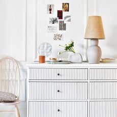 White ribbed chest of drawers with lamp, mirror and vase