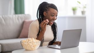 Woman eating popcorn while watching something on her laptop