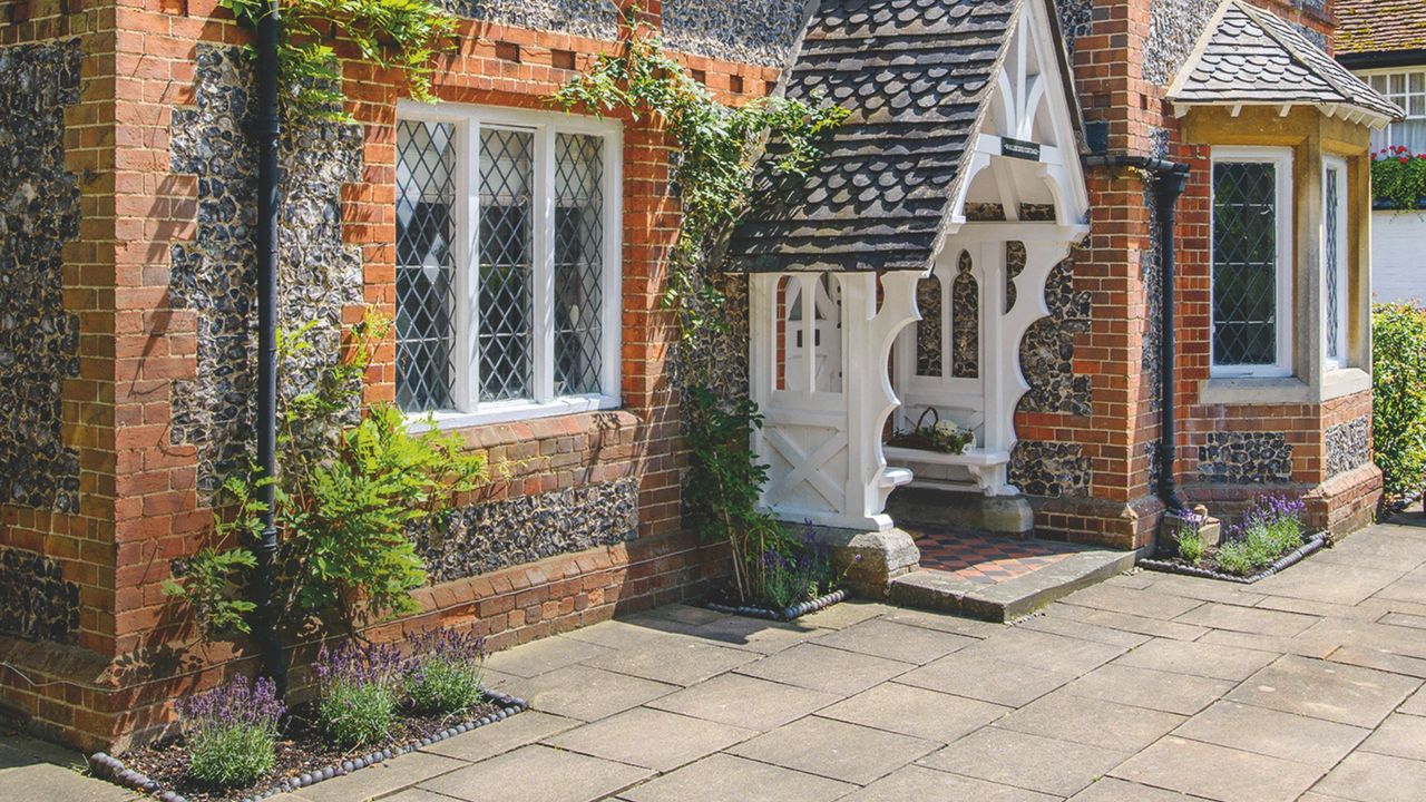 Front of brick and flint Grade II listed former Victorian school house with flowering lavender plants and wall climbing plants