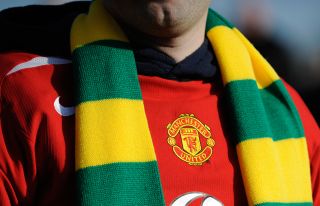 A close-up of a fan wearing a Manchester United shirt, and a scarf in yellow and green - the colours of the club under their original guise of Newton Heath