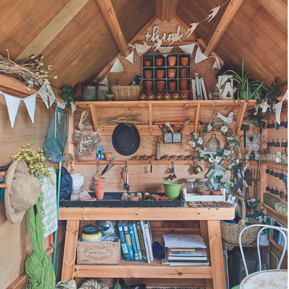 Wooden potting bench inside shed with shelves, garden tools, pots and hats