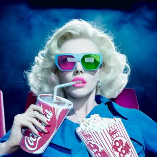 A woman wearing 3d glasses and holding a cardboard cut out of popcorn and coca-cola