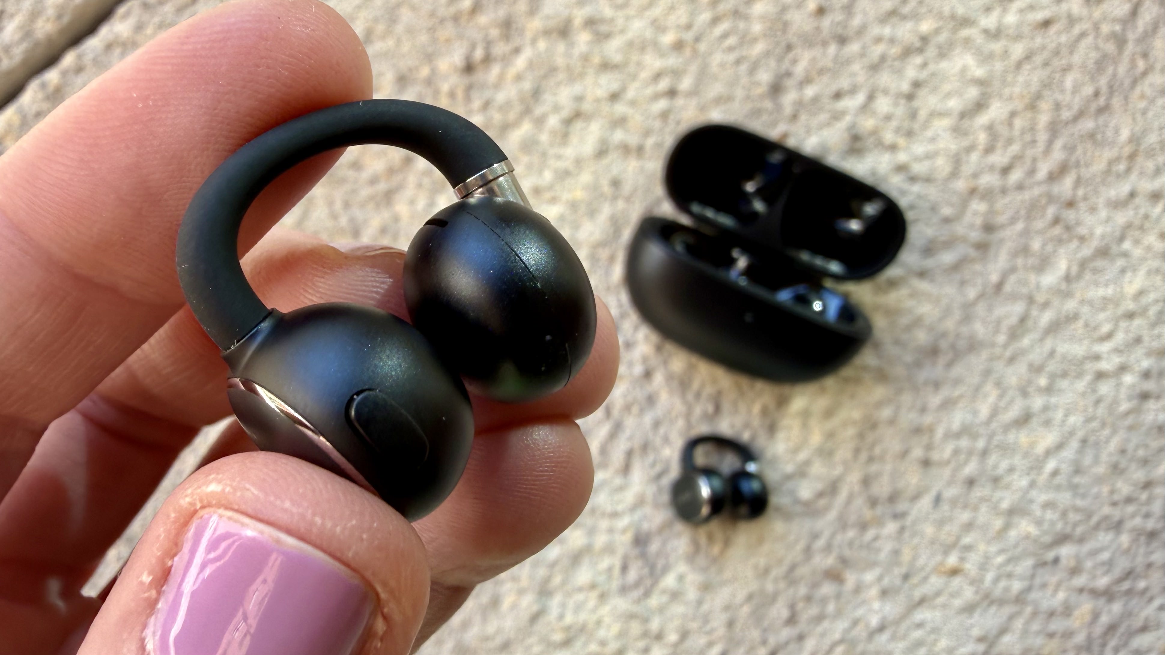 Someone holding one of the EarFun Clip 2 earbuds