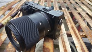 Photograph of Sony A6000 camera on metal table with 30mm lens and wrist strap: Sony A6000 review