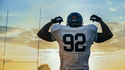 A football player flexes his biceps against a backdrop of a beautify sunset.