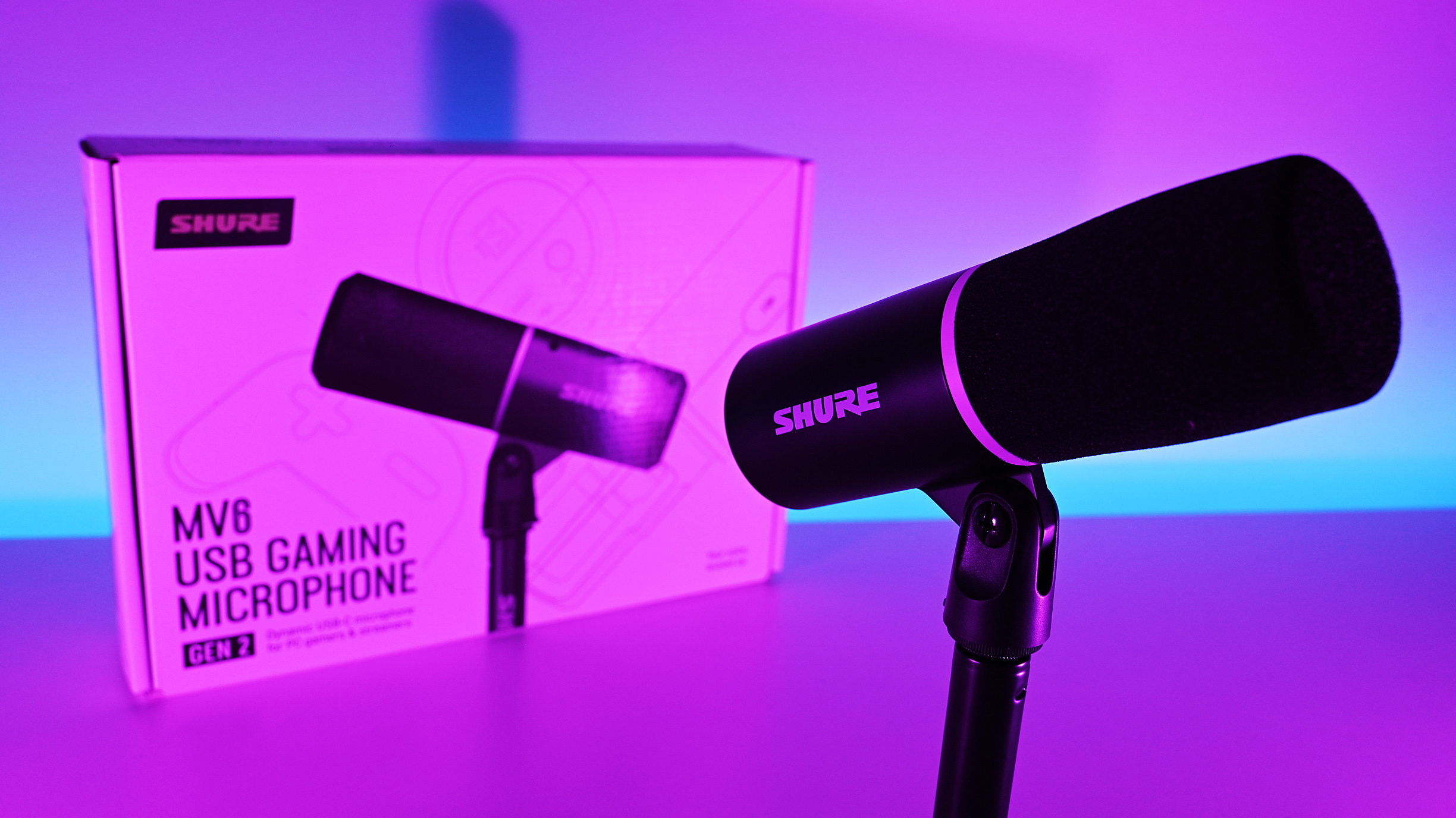 Shure MV6 Gen 2 microphone and retail box illuminated under vibrant pink and purple studio lighting.