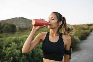 Training tips for a marathon: A woman drinks water while out on a run