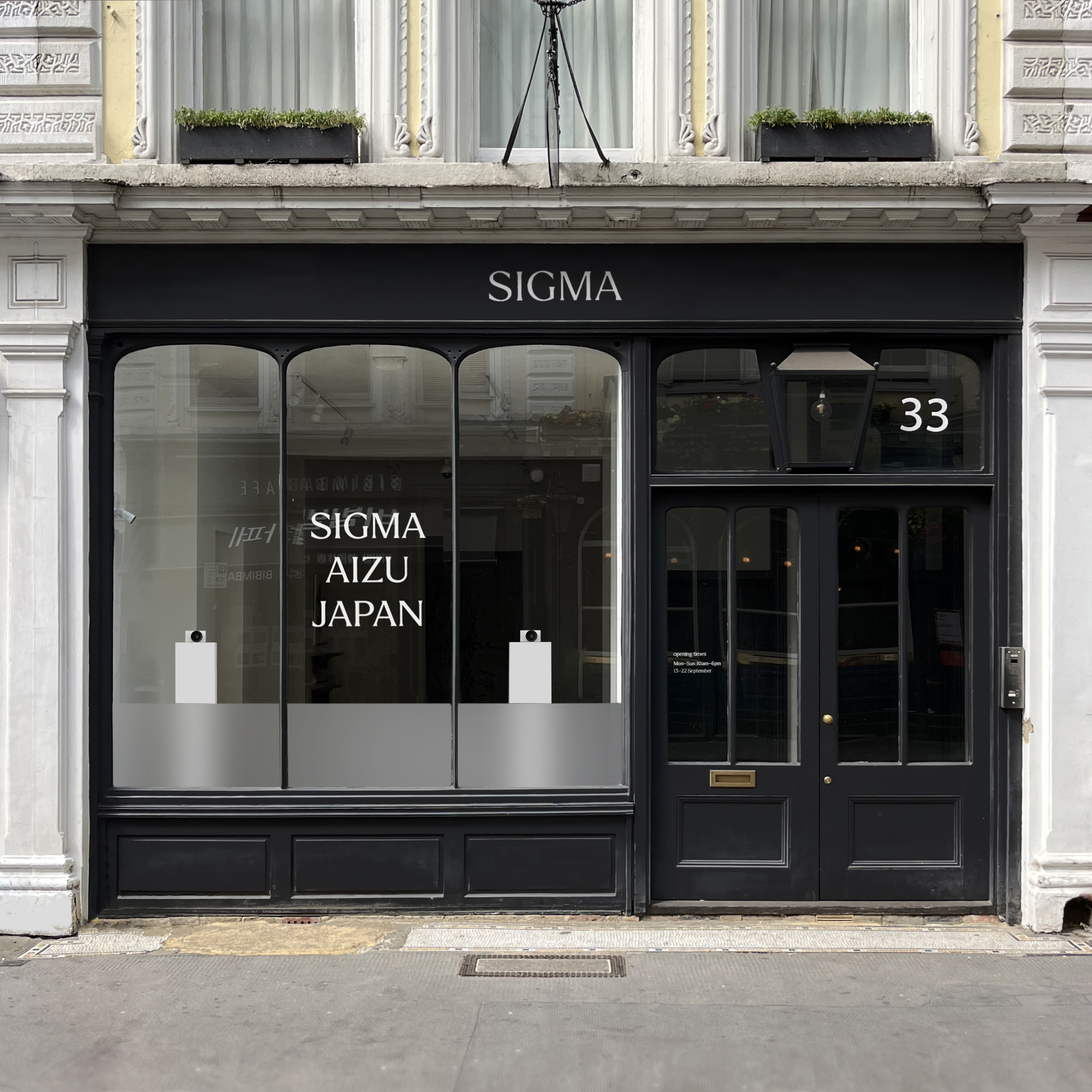 Facade of the Sigma shop featuring large windows displaying &quot;SIGMA AIZU JAPAN&quot; and minimalist white pedestals, located at number 33.