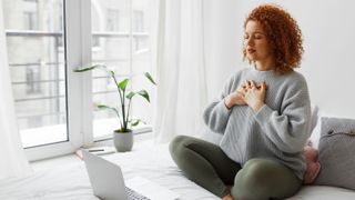 a woman sat cross legged on a bed taking in a deep breath