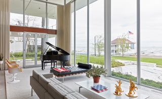 Living room with large floor to ceiling windows, grey sofa, chaise lounge and baby grand piano