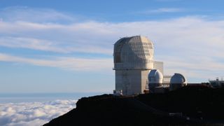 A white building with dark domed roofs sits on a dark surface