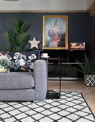 A black living room with Berber-style cream rug, grey upholstered sofa with floral cushions, houseplant in geometric planter, brass-framed wall art, slogan neon light and decorative LED star