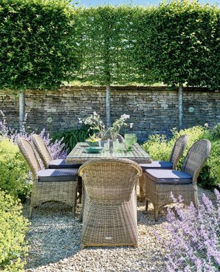 Outdoor dining area next to rustic stone wall with pleached trees