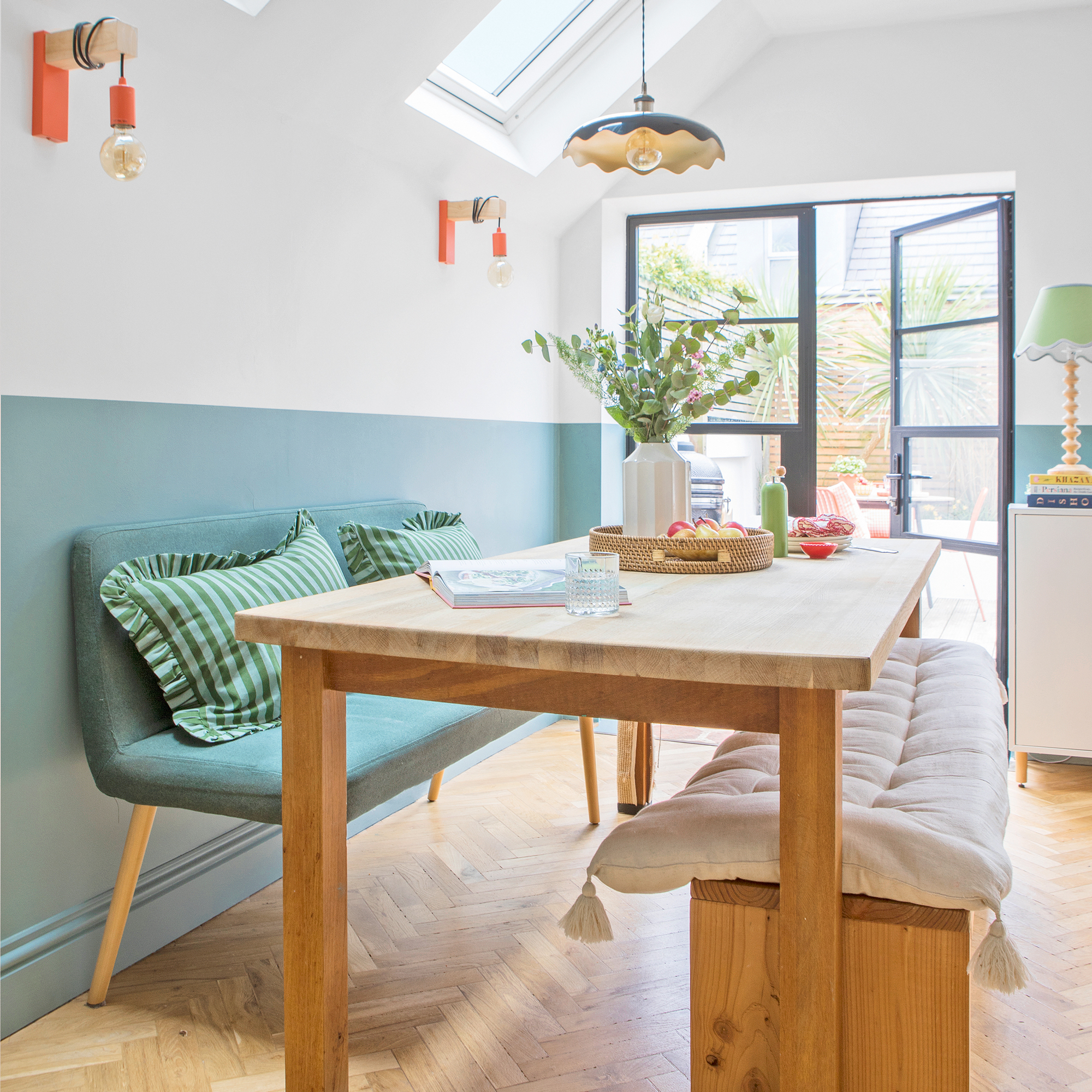 a dining area that leads out to a garden via patio doors with a blue painted half wall and dining table and benches