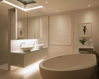 A white bathroom with a large white bath and two white sinks lit from above