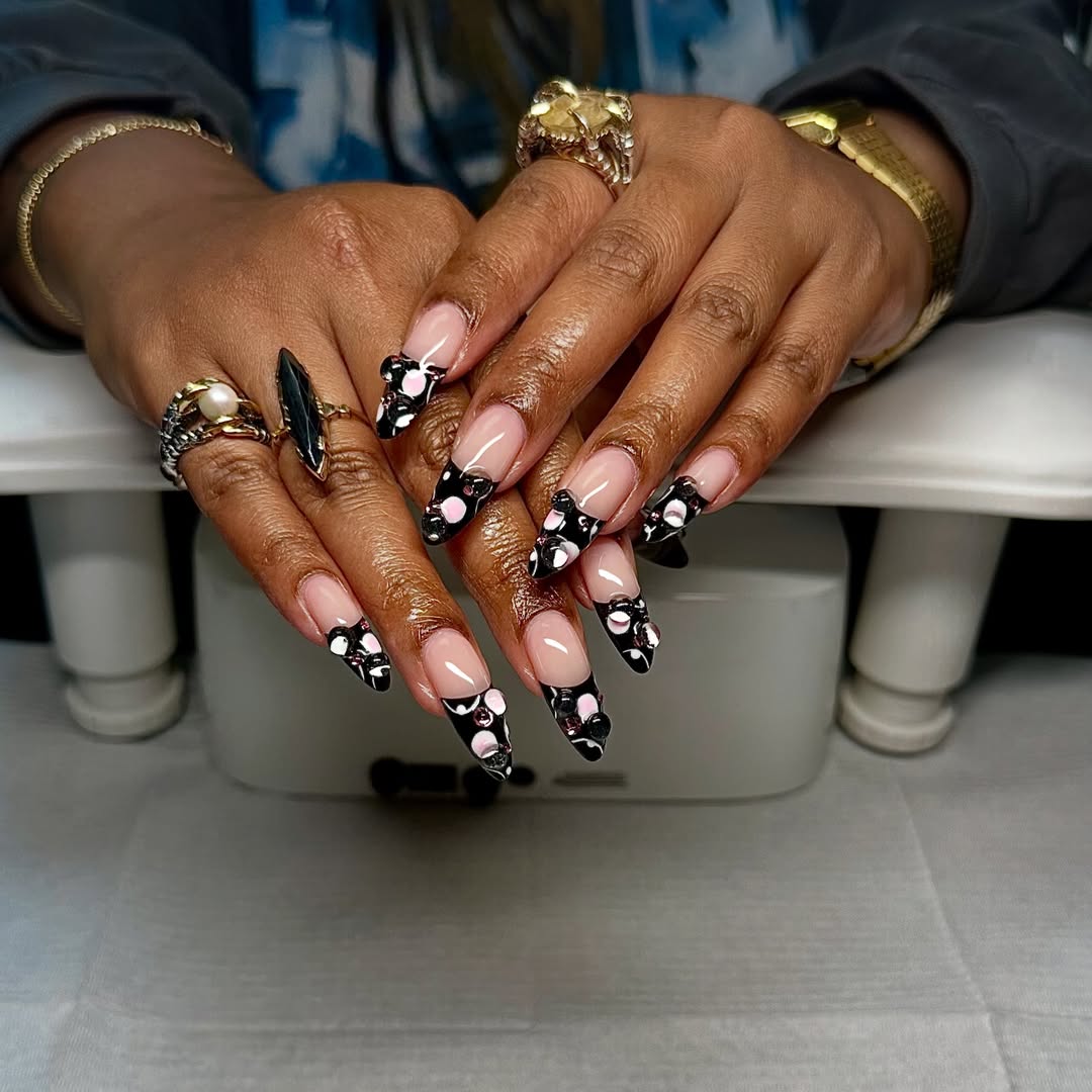 a person with long nails wearing a black french manicure with pink polka dots and 3D gel